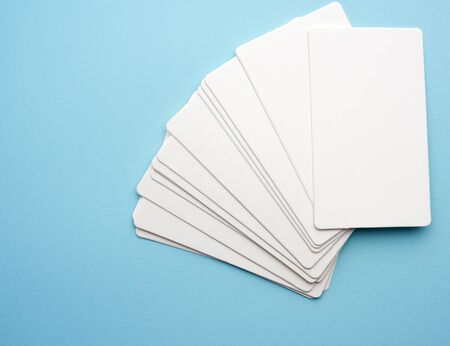 stack of rectangular white paper blank business cards on blue background, top view, close up
