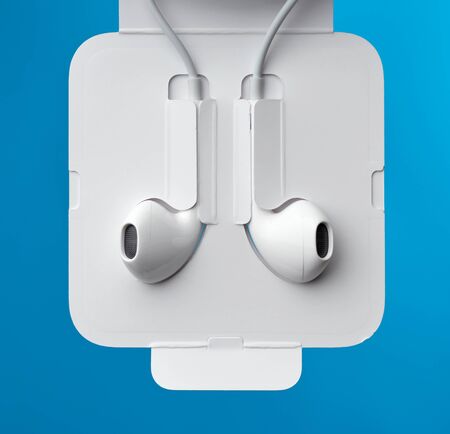hanging headphones on a white cable, a modern gadget on a blue background, close up, product is...