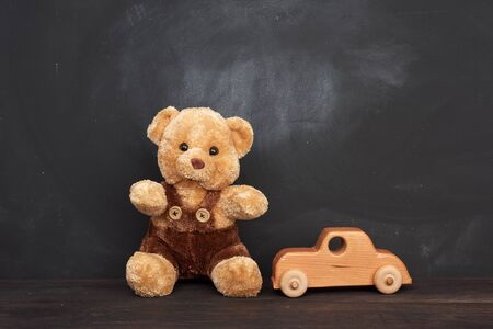 brown teddy bear sits on a brown wooden table and wooden car, behind an empty black chalk board, place for an inscription, back to schoolの写真素材