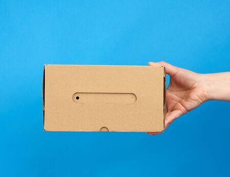 hand holds a brown cardboard box of paper on a blue background, close upの写真素材