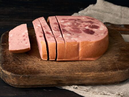 sliced boiled sausage with slices of whole meat on a brown wooden cutting board, close upの写真素材