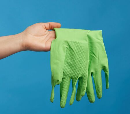 female hand holds green rubber gloves for cleaning, blue background, protective clothing for house cleaningの写真素材