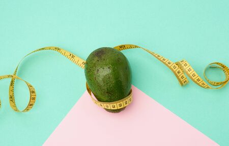 green avocado fruit and a twisted measuring yellow tape on a green pink background, diet and weight loss concept, top viewの写真素材