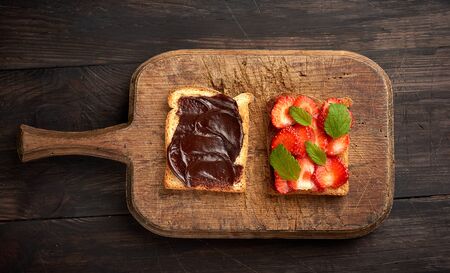 two toasts with chocolate paste and fresh ripe red strawberries on a brown wooden board, top view, morning breakfastの写真素材