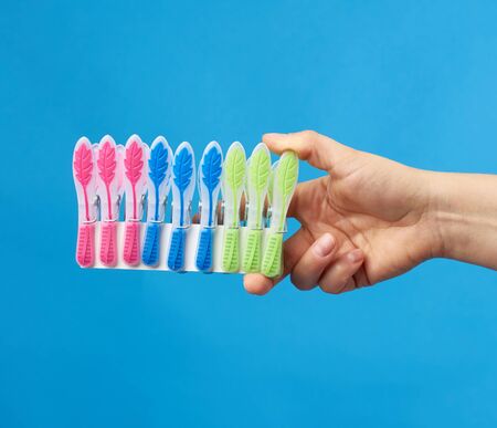 hand holds a stack of multi-colored plastic clothespins on a blue backgroundの写真素材