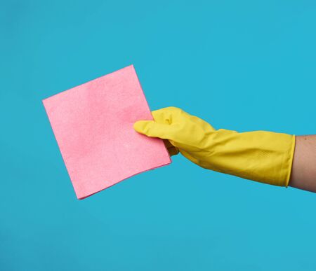 yellow rubber glove for cleaning is put on his hand and holds a kitchen pink sponges on a blue...