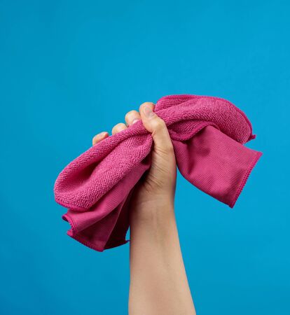 hand holds pink textile rag for cleaning, blue background