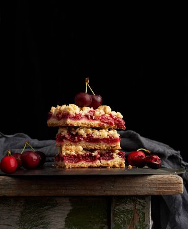 stack of square slices of a pie with red cherry, black background, delicious crumbleの写真素材