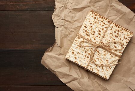bandaged stack of baked square matzoh on brown paper, top view, copy space