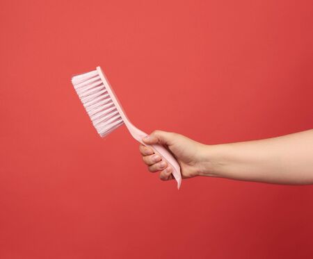 female hand holds pink plastic cleaning brush, red backgroundの写真素材