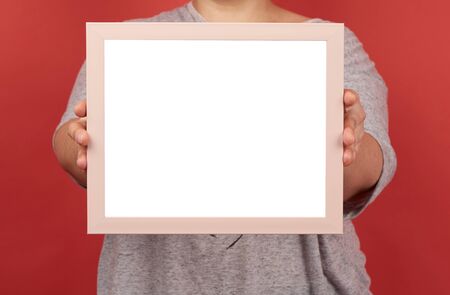 woman holds an empty pink frame on a red background, place for an inscriptionの写真素材