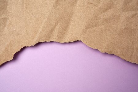 crumpled sheet of brown wrapping paper with torn edges on a purple background, backdrop for the designerの写真素材
