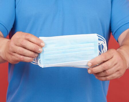 man in a blue T-shirt holds a stack of disposable medical white face masks. the concept of using...
