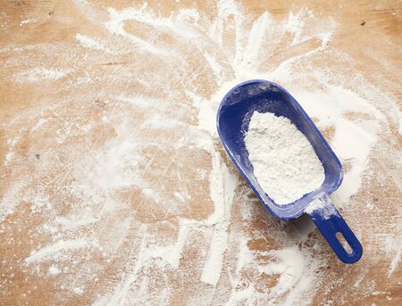 white wheat flour scattered on a brown wooden table and blue plastic scoop, top viewの写真素材
