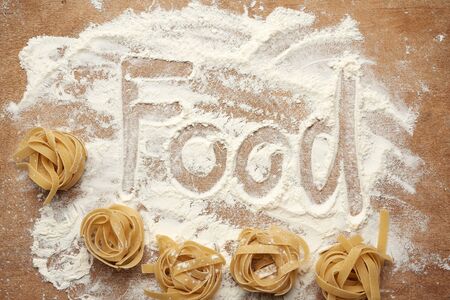 raw fettuccine pasta on a brown wooden board with white flour, top viewの写真素材