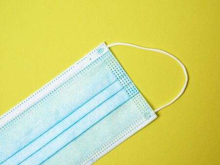 blue disposable medical mask on a yellow background, personal protective equipment for the respiratory tract from viral infections, top viewの写真素材