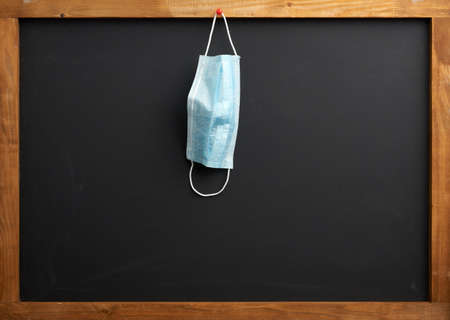 empty black school chalk board, a disposable medical mask hanging on a red button, the concept of...