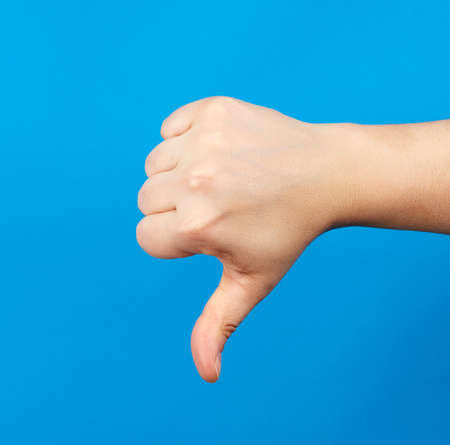 female hand shows fist gesture and thumb down, dislike, part of the body on a blue backgroundの写真素材