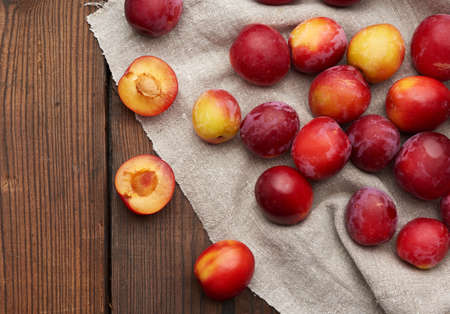 ripe red plums on a gray linen towel, brown wooden table, top viewの写真素材