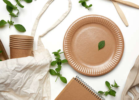 textile bag and disposable tableware from brown craft paper, green mint leaves on a white background. View from above, plastic rejection concept, zero wasteの写真素材