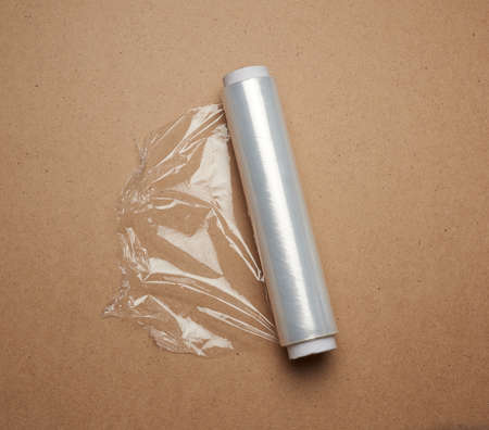 big roll of wound white transparent film for wrapping food, brown wooden background, top view