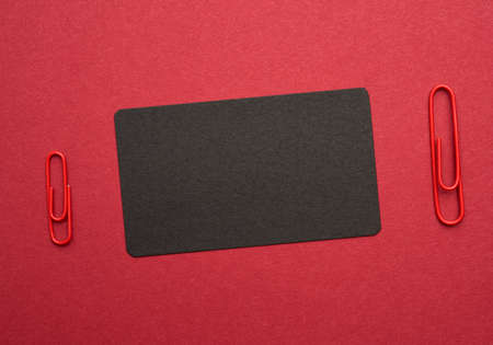 black paper cardboard business card and red metal paper clip on a red background, top view, flat layの写真素材