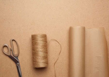 brown craft paper roll, skein of thread and scissors on a brown wooden background, top viewの写真素材