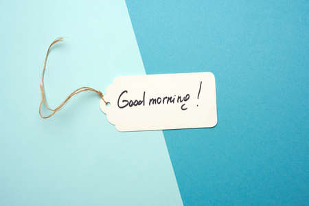 white paper tag with brown rope and the inscription good morning, blue background