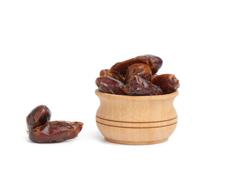 heap of dried dates in a wooden bowl and isolated on a white background, close upの写真素材