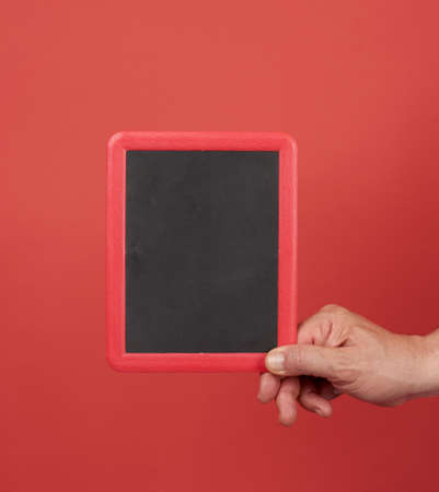 hand holding an empty frame on a red background, place for an inscription