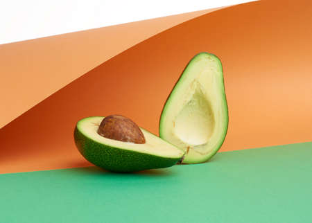 half ripe green avocado with a brown bone on an abstract green-orange background with curved paper