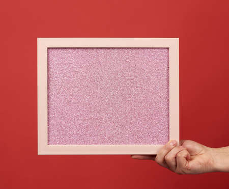 woman holds an empty pink frame on a red background, place for an inscriptionの写真素材