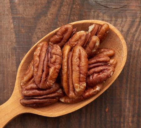 peeled pecans in a brown wooden spoon on a brown wooden background, top view