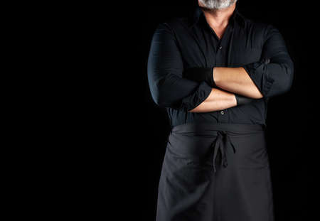male chef in black uniform crossed his arms in front of his chest on a black background, banner for restaurants and cafes, empty space for an inscriptionの写真素材