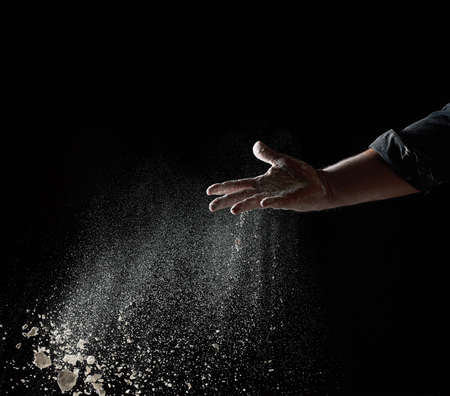 baker's hand throws a handful of white wheat flour on a black background, the particles fly in different directionsの写真素材