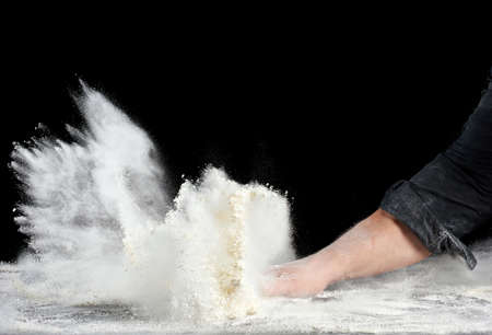 chef in black uniform sprinkles white wheat flour in different directions, product scatters dust, black background, particles scatter and freeze in the airの写真素材