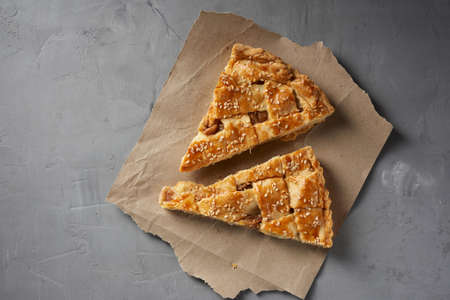 two baked pieces of apple pie on brown paper, top view, gray background