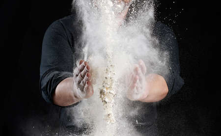 chef in black uniform sprinkles white wheat flour in different directions, product scatters dust,...