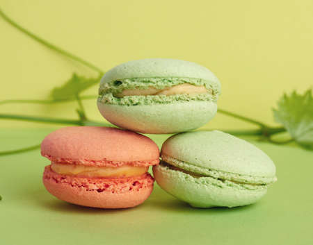 three round multi-colored baked macarons, the dessert lies on top of each other on a green...