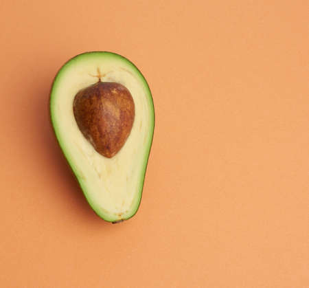 half ripe green avocado with a brown bone on an abstract orange background, top viewの写真素材