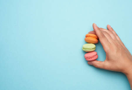 female hand holds three round baked macarons cookies on a blue background, place for an inscription, top viewの写真素材