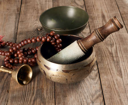Tibetan singing copper bowl with a wooden clapper on a brown wooden table, objects for meditation and alternative medicine, close upの写真素材