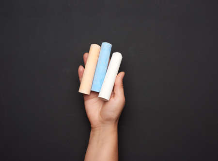 female hand holding three colored chalk on a background of an empty black chalk board, close upの写真素材