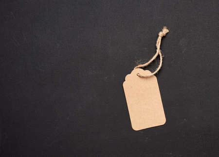 empty paper brown rectangular price tag on a rope on a black background, copy spaceの写真素材
