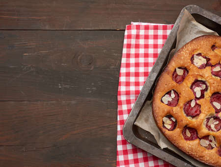 baked sponge cake with plums in a metal baking sheet on a brown wooden background, top view, copy spaceの写真素材