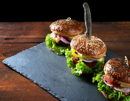 three delicious burgers with fried beef cutlet, tomato, lettuce and onions, crispy white wheat flour bun with sesame seeds. Fast food on a wooden boardの写真素材