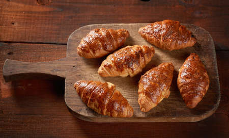 baked croissants on a wooden brown board, delicious and appetizing pastries, top view