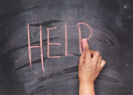 female hand with red chalk writes help on a black chalk board, close upの写真素材