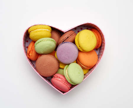 round baked multicolored macarons lie in a red cardboard box in the shape of a heart on a white background, top viewの写真素材