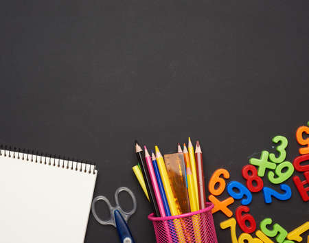 colorful wooden pencils, notepads on a blank black chalk board, school stationery, copy space, back...